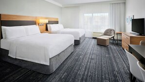 Een hotelkamer met twee bedden, een bureau, een stoel, een televisie en een raam met gordijnen.