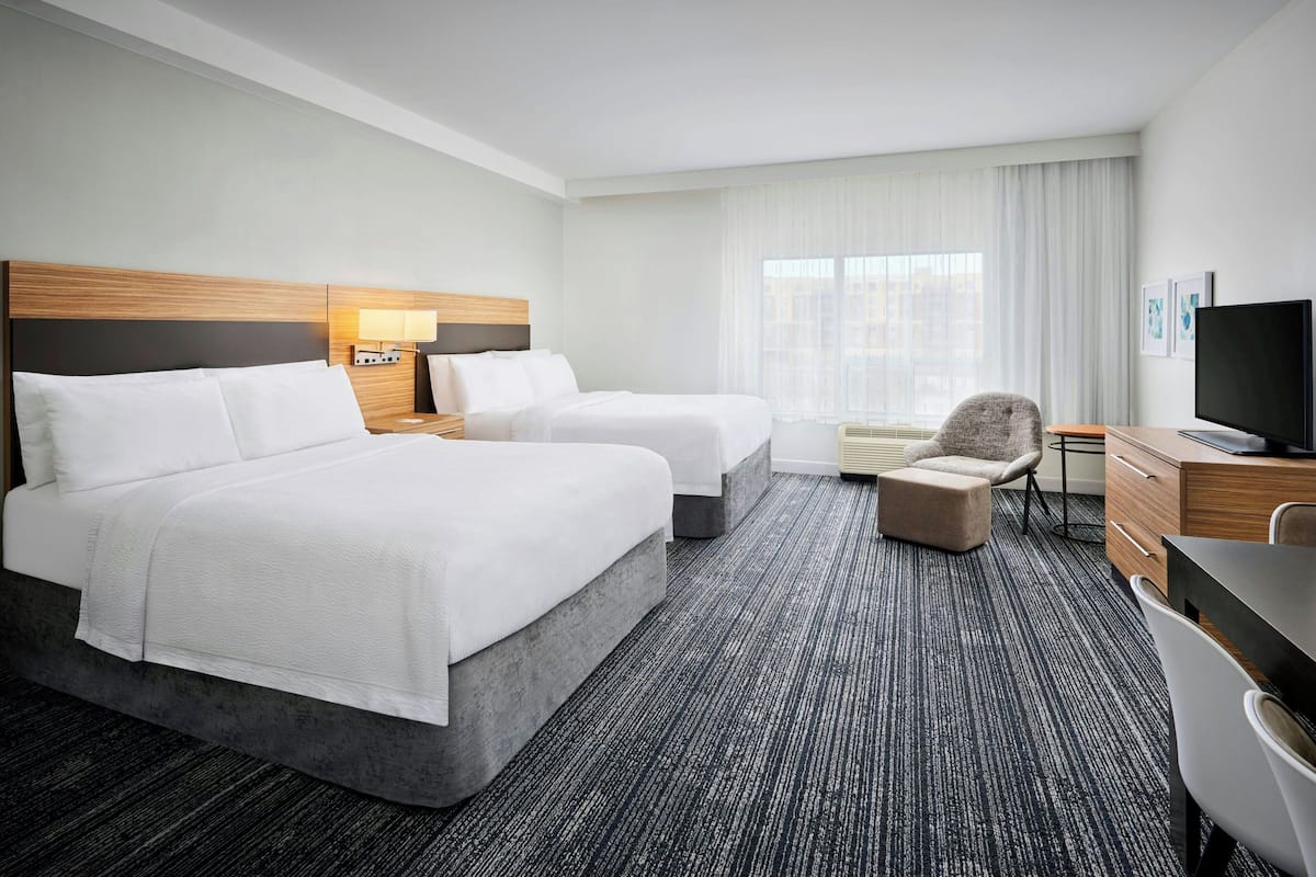 Une chambre d’hôtel avec deux lits, un bureau, une chaise, une télévision et une fenêtre avec des rideaux.