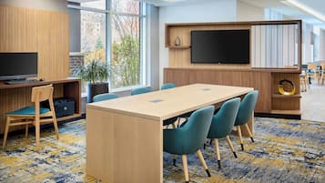 Una sala de reuniones moderna con una mesa larga, sillas azules, un televisor y un ventanal grande.