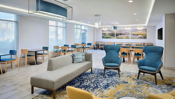 Een moderne hotellobby met een bank, stoelen, een eetgedeelte en een groot raam met uitzicht op de stad.