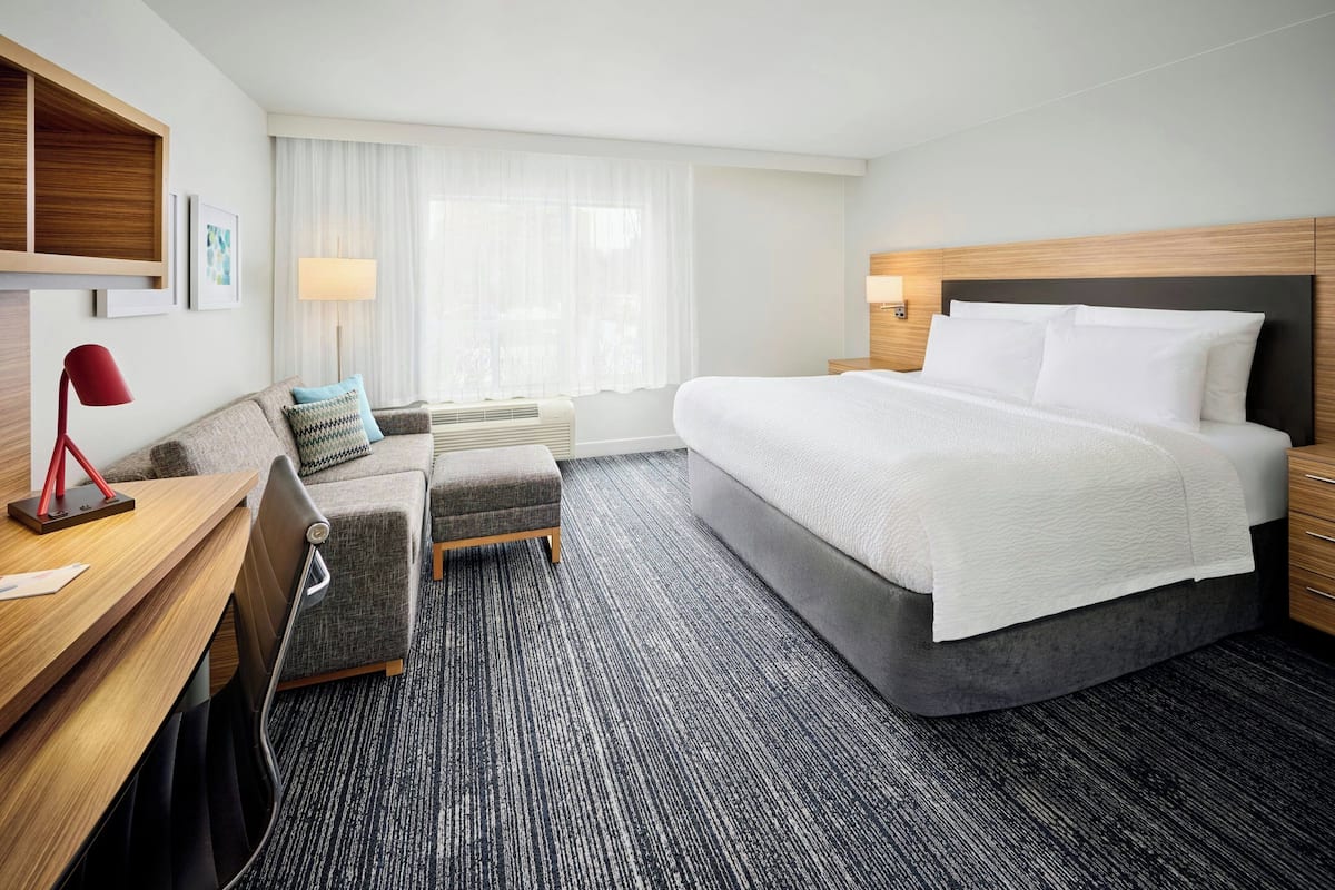 Une chambre d’hôtel équipée d’un lit, d’un bureau, d’une chaise, d’un canapé, d’une lampe et d  ’une fenêtre avec des rideaux.