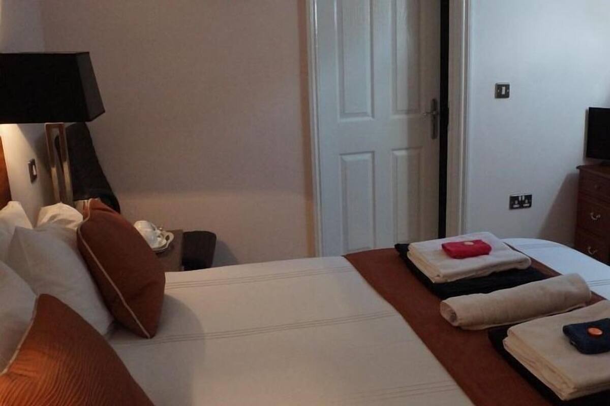 A hotel room with a bed, pillows, a bedside table, a lamp, and a door.