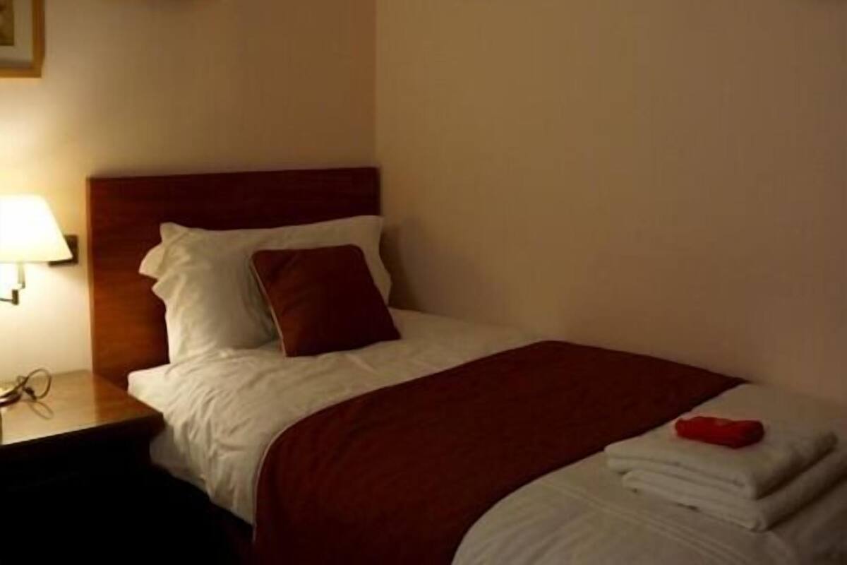 A hotel room with a bed, a nightstand, a lamp, and a framed picture on the wall.