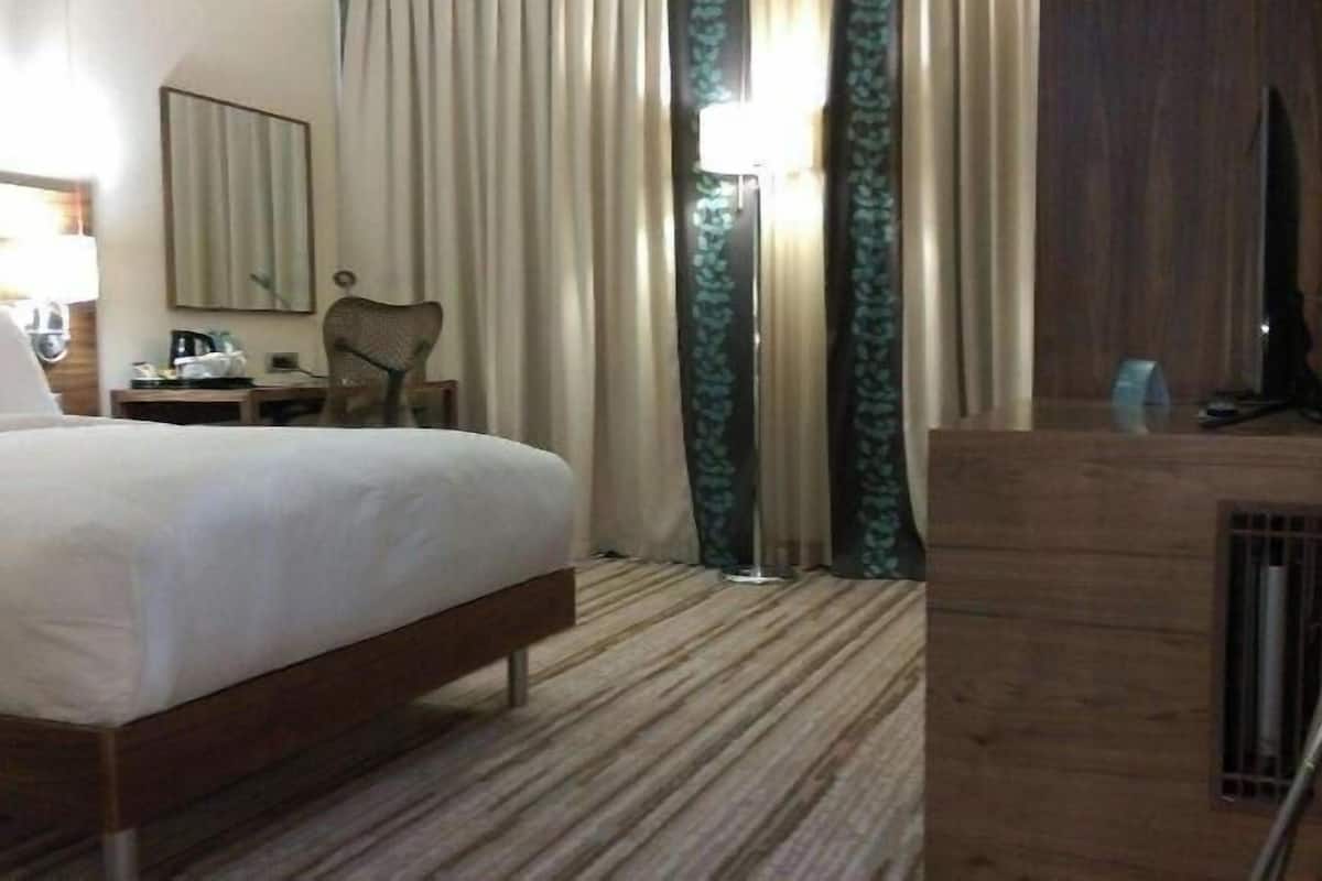 A hotel room with a bed, a desk with a lamp, a chair, a television, and a window with curtains.