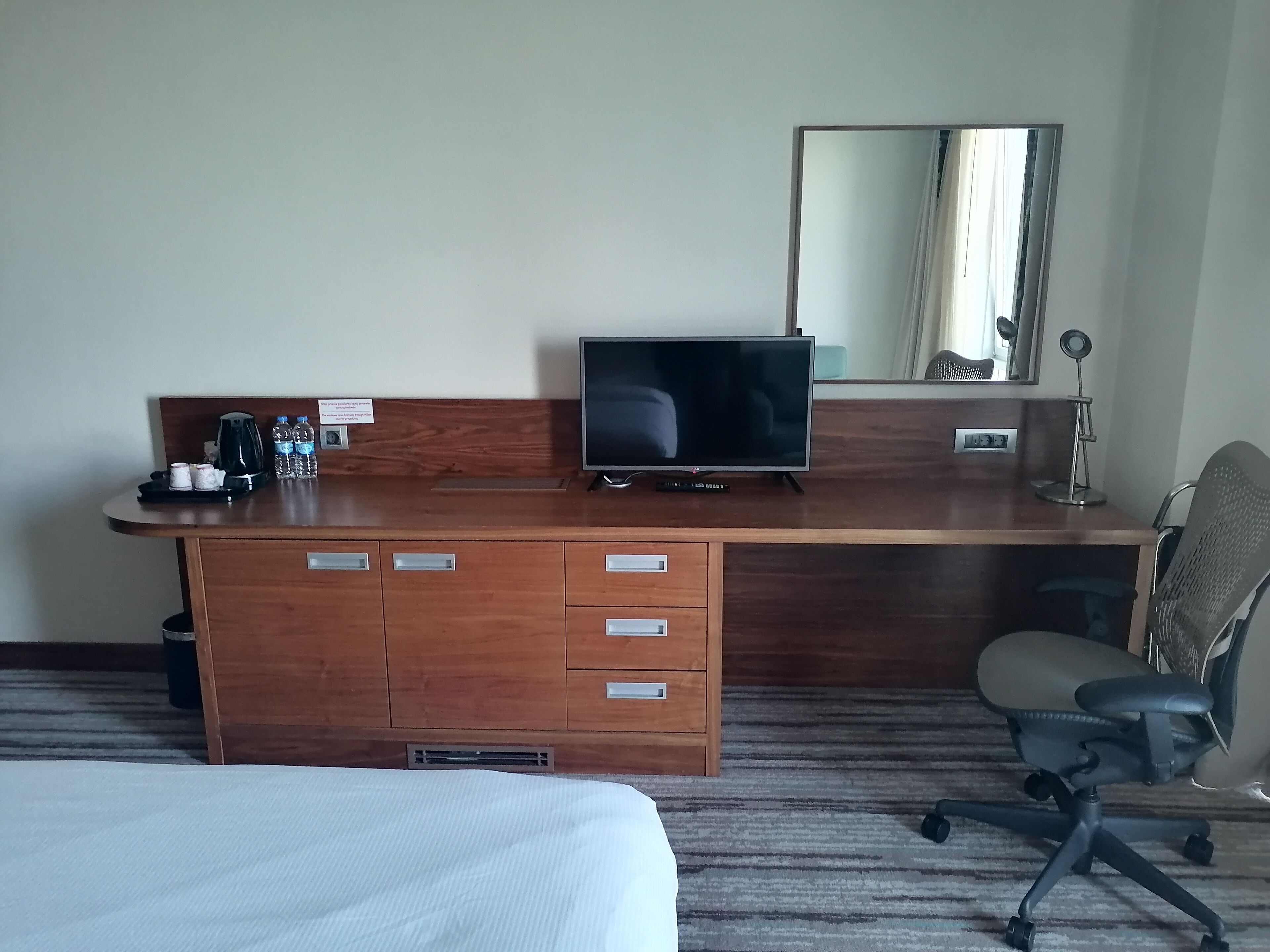 Habitación de hotel con escritorio de madera, televisión de pantalla plana, silla, cama y un espejo grande.