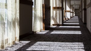 A long, narrow hallway with a carpeted floor, large windows with sheer curtains, and a ceiling with recessed lighting. - Hilton Garden Inn Erzincan (Erzincan)