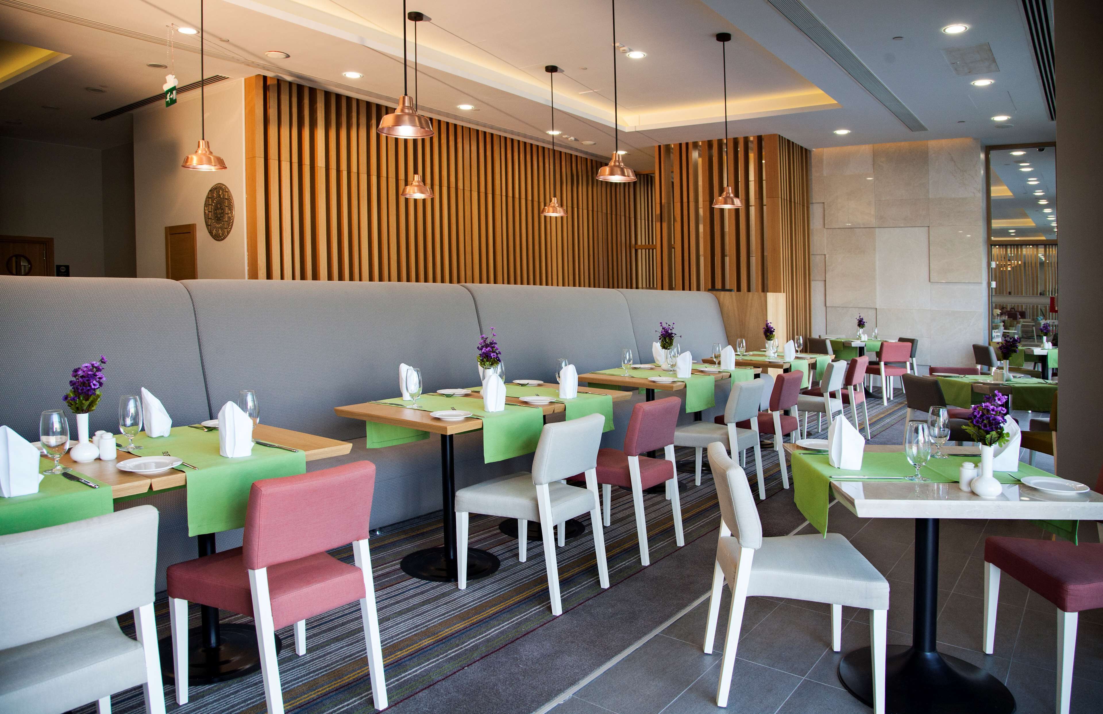 A modern restaurant with booths and tables, green and white tablecloths, and pendant lighting.