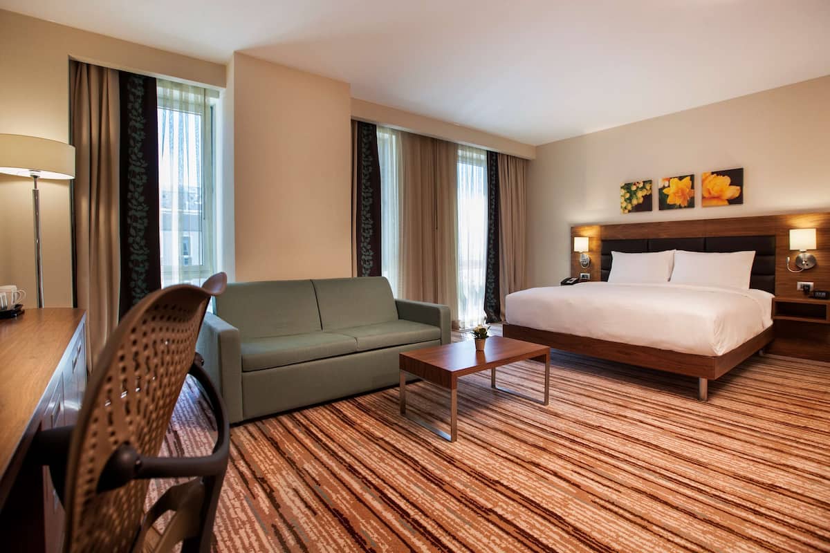 A hotel room with a bed, a sofa, a coffee table, and a desk with a lamp.