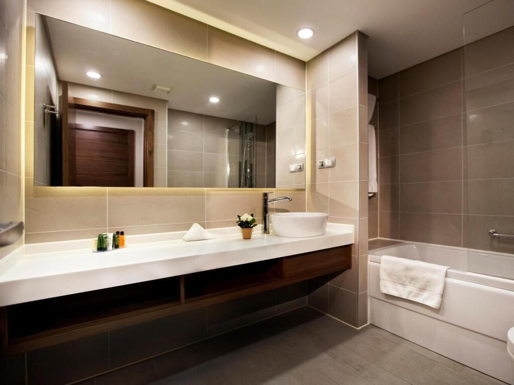 Une salle de bain moderne avec un grand miroir, deux lavabos, une baignoire et un meuble-lavabo en bois.