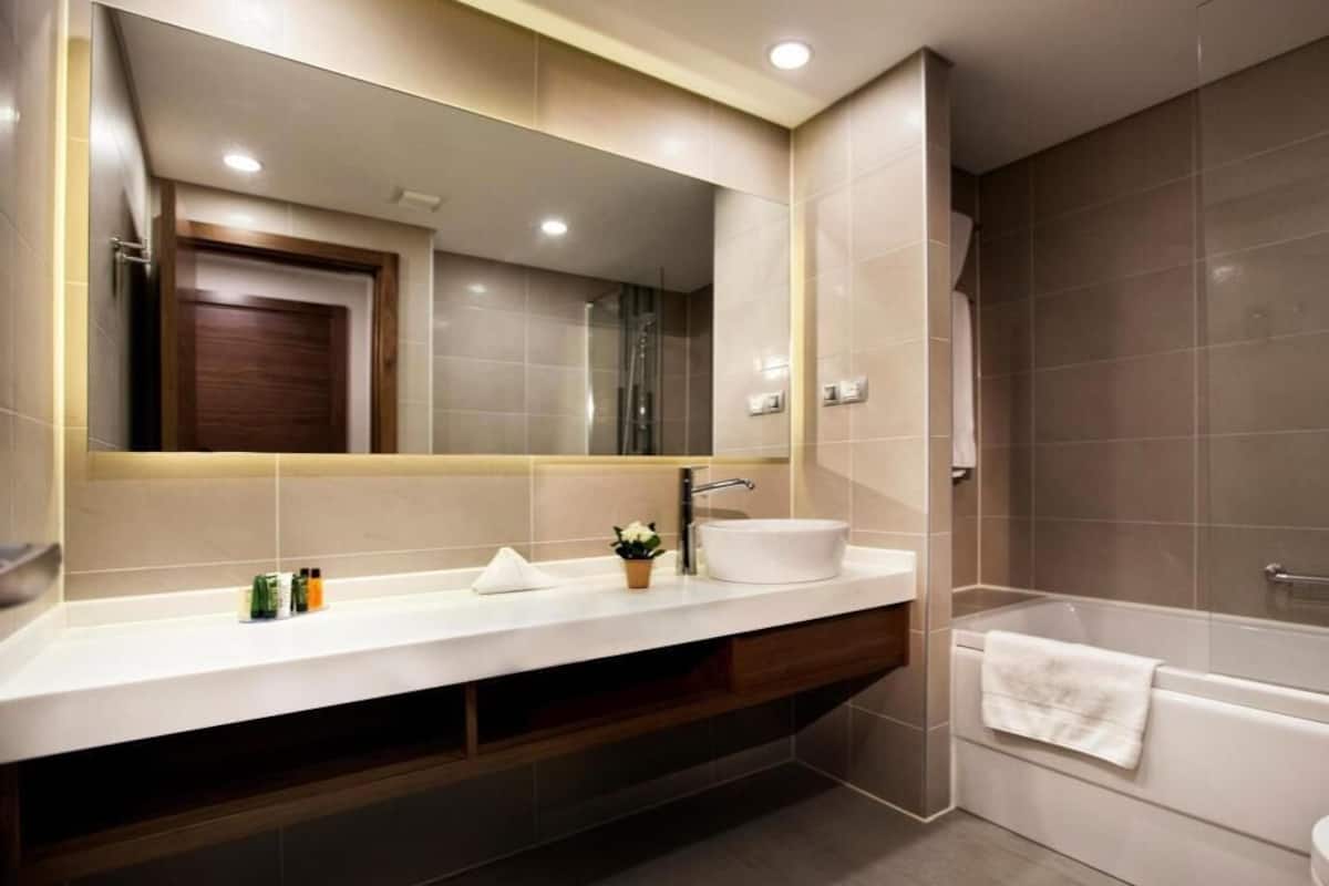 A modern bathroom with a large mirror, two sinks, a bathtub, and a wooden vanity.
