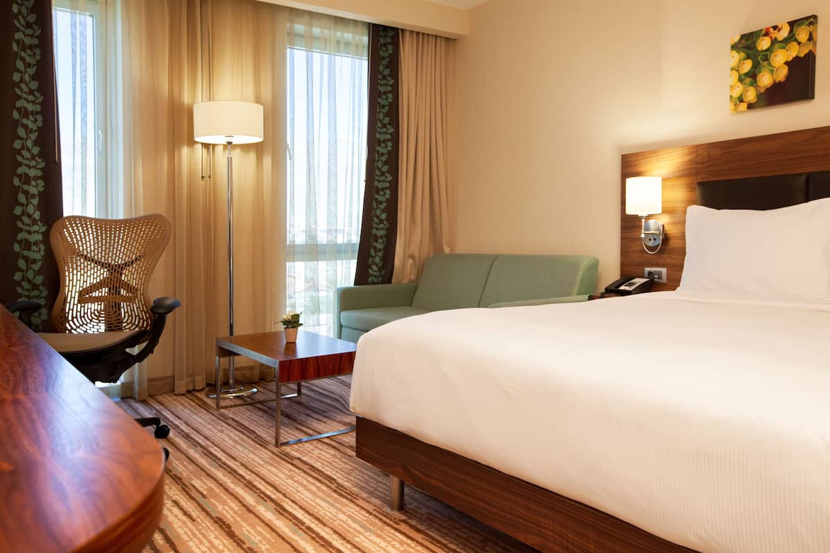 A hotel room with a large bed, a desk, a chair, a lamp, and a window with curtains.