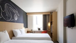 A hotel room with two beds, a desk with a chair, a TV, and a large window with curtains. - ibis México Alameda (Mexico City)