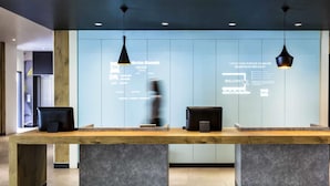 A reception desk with a wooden top and two black pendant lights. There are two black speakers on the desk. - ibis México Alameda (Mexico City)