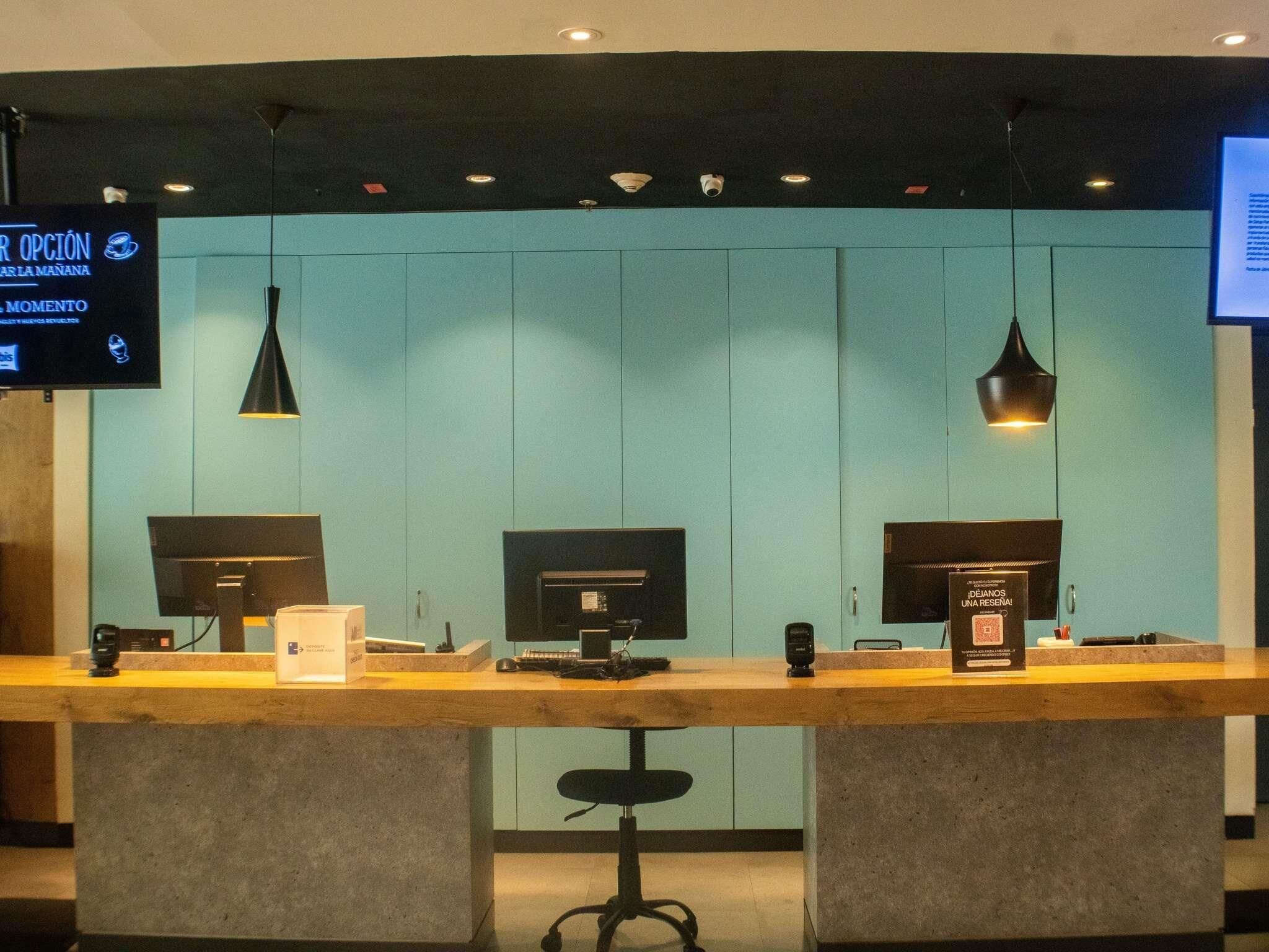 A reception desk with two computer monitors, a coffee machine, and a sign indicating a moment for something.