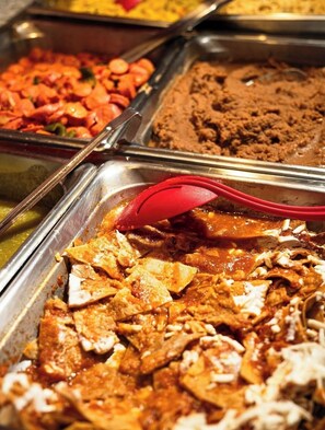 A buffet with various dishes including a red sauce, shredded chicken, and a brown dish.
