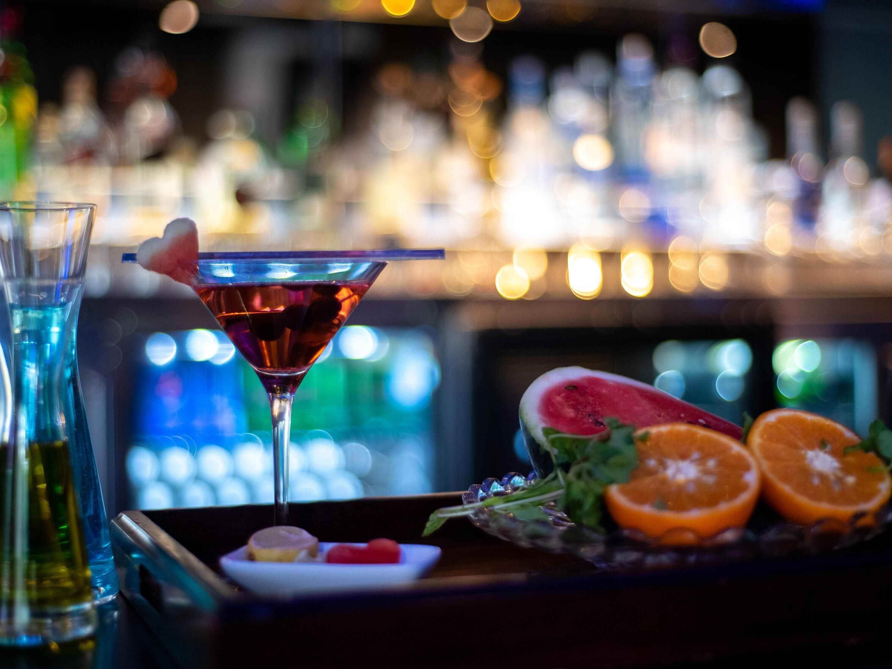 A bar setting with a martini glass, a watermelon slice, and an orange slice on a tray.