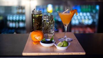 Un bar avec un cocktail, une planche en bois sur laquelle est posée une tranche de citron vert, un bol d’olives et deux bocaux en verre.