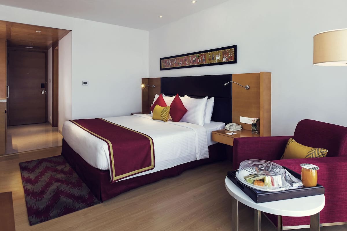 Une chambre d’hôtel avec un lit, une table de chevet, une chaise et une petite table sur laquelle se trouvent un plateau de nourriture et une tasse de café.