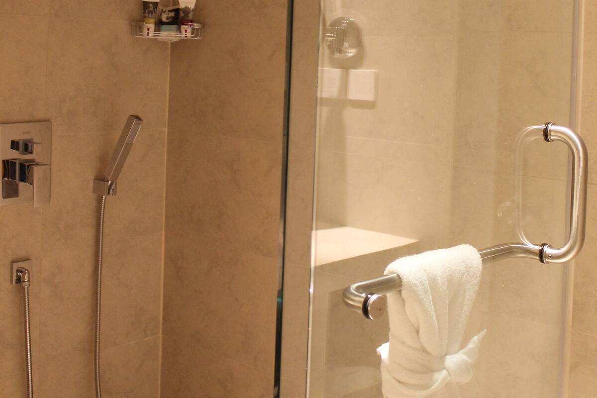 Un espace douche fermé par des parois en verre, doté d’un pommeau de douche à main, d’un porte-serviettes avec une serviette et d’une petite étagère contenant des articles de toilette.