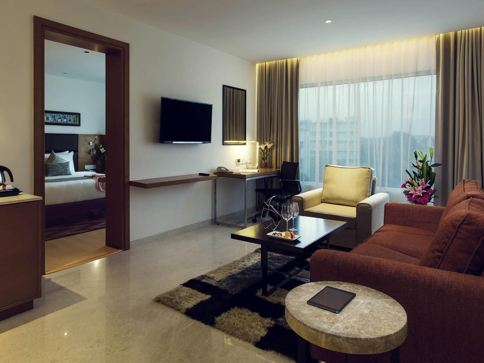 A modern hotel room with a bed, a sofa, a coffee table, a TV, and a desk with a chair.