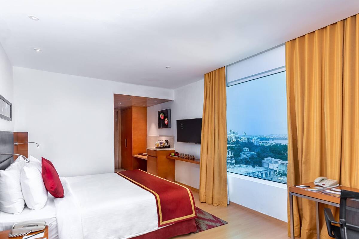 Une chambre d’hôtel avec un lit, un bureau et une grande fenêtre donnant sur la ville.