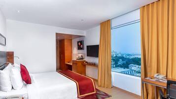 Habitación de hotel con cama, escritorio y un amplio ventanal con vista a la ciudad.