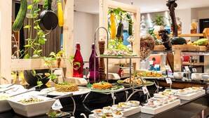 En buffet med forskellige retter, træhylder med planter og et moderne køkken i baggrunden.