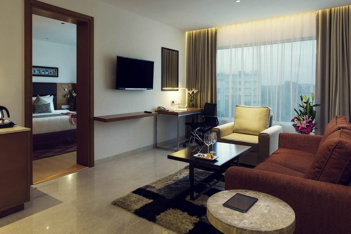 Une chambre d’hôtel moderne équipée d’un lit, d’un canapé, d’une table basse, d’une télévision et d’un bureau avec une chaise.