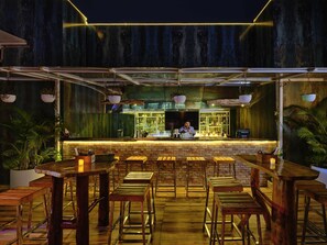 Un área de bar al aire libre con taburetes de madera, una barra y un barman.