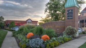 A landscaped area with a brick wall, a sign for 'Levis Commons', and a building with a green roof. - Holiday Inn Express & Suites Toledo South - Perrysburg by IHG (Perrysburg)