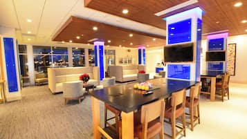 Een moderne hotel lobby met een bar, zitplaatsen en een groot raam met uitzicht op de stad.