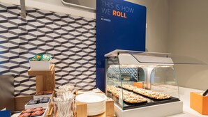 A breakfast buffet area with a display of cinnamon sweet rolls, a sign indicating the roll selection, and a patterned wall in the background. - Holiday Inn Express & Suites Toledo South - Perrysburg by IHG (Perrysburg)