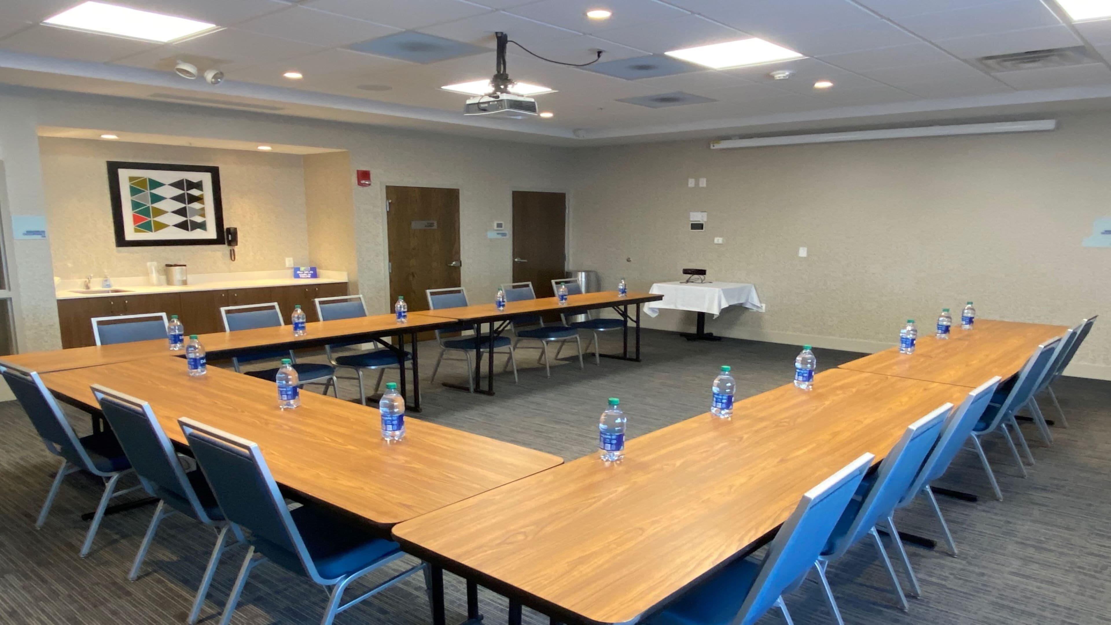 Un salón de conferencias con una larga mesa, sillas, botellas de agua, un proyector y una pizarra.