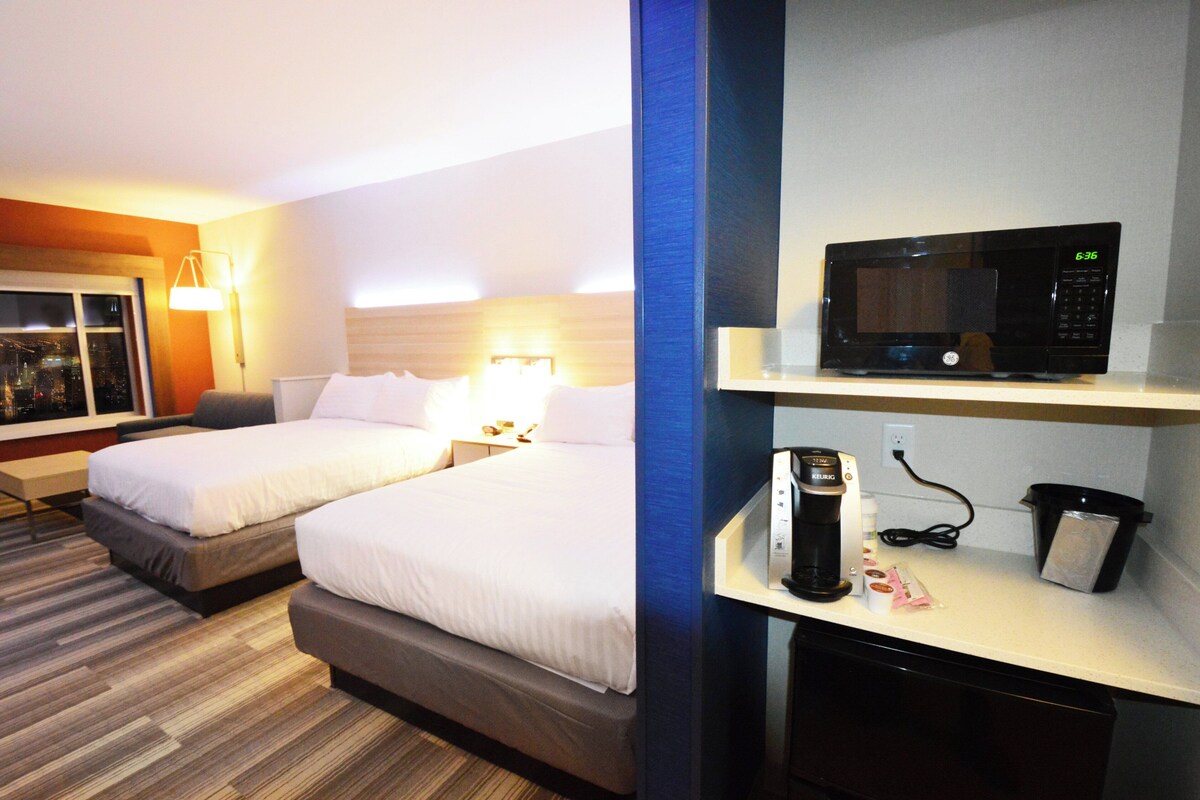 Habitación de hotel con dos camas, microondas, cafetera y un cubo de basura.