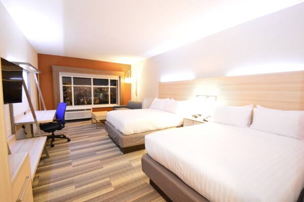 Habitación de hotel con dos camas, un escritorio, una silla, un televisor y una ventana con vista a la ciudad.