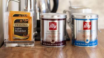 Una cafetera, dos recipientes para café y un paquete de café Twinings English Breakfast sobre una superficie de madera.