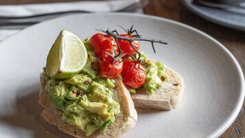 Un plato con tostada de aguacate, tomates cherry y un gajo de lima.