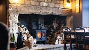 A stone fireplace with a wood-burning stove, a dining table with chairs, and a stone wall.