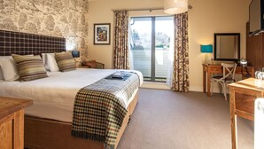 A bedroom with a large bed, a desk, a chair, a lamp, a mirror, and a view of the outdoors through a sliding door.