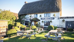A traditional white building with a thatched roof, named "The White Hart," featuring outdoor wooden picnic tables and a signboard.