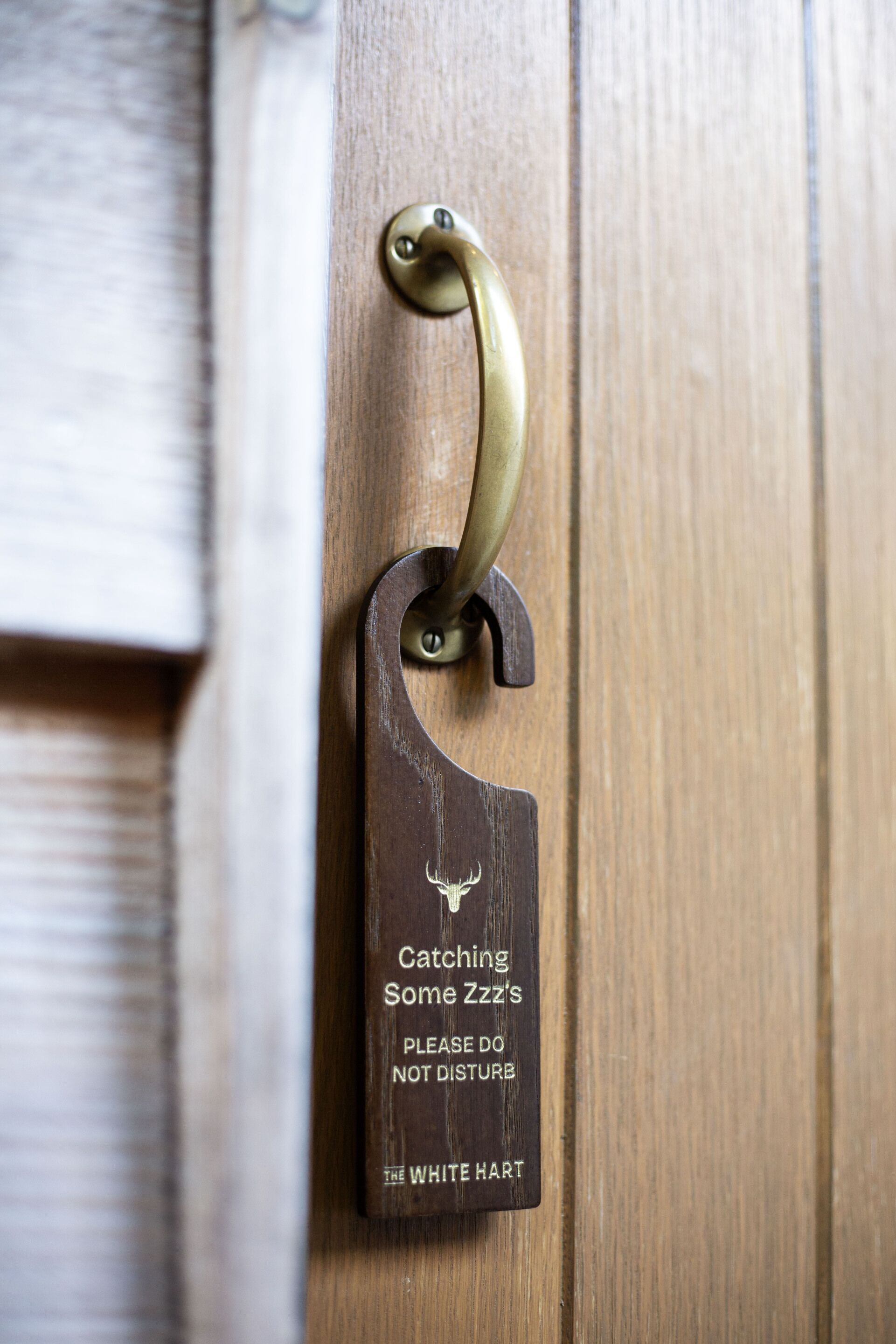 A wooden door with a brass doorknob and a sign that reads "Catching Some Zzz's Please Do Not Disturb The White Hart."