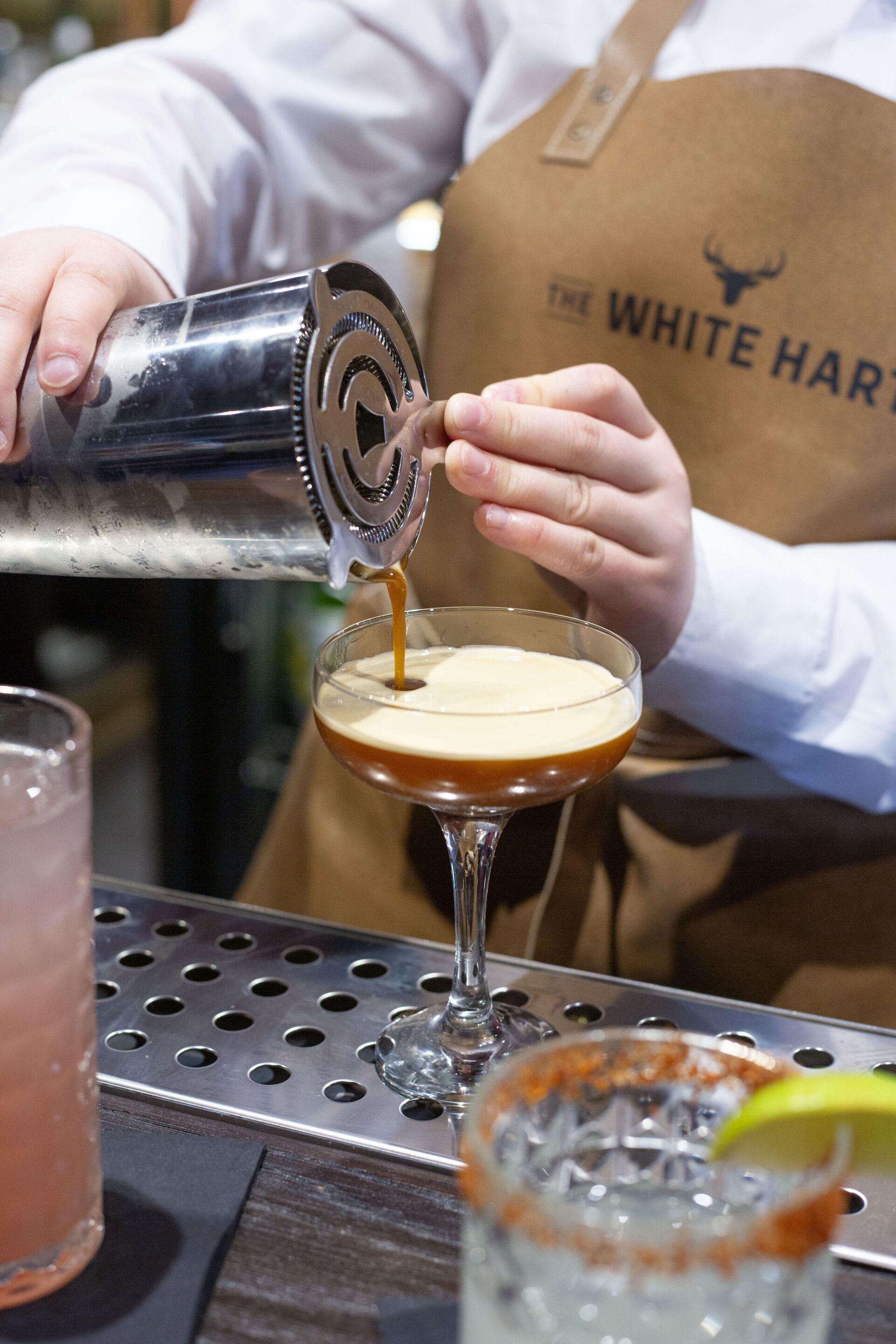 A bartender pouring a drink into a martini glass.