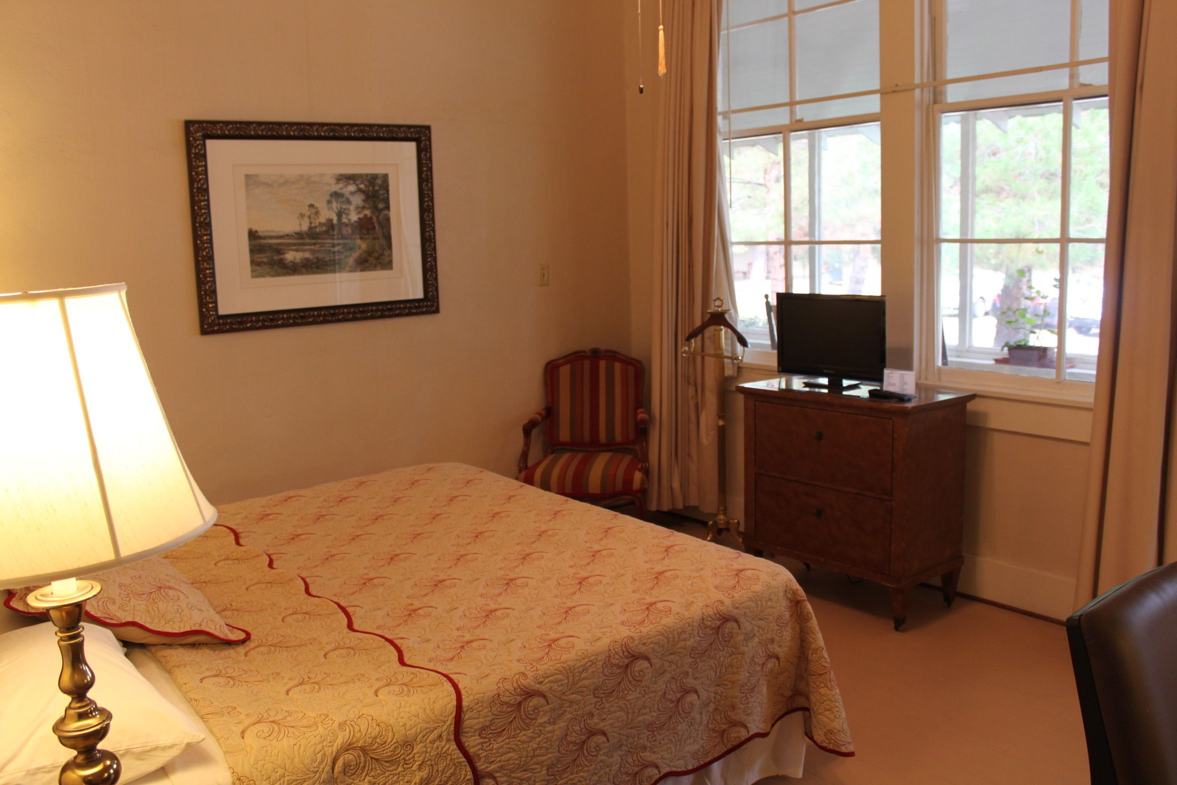 Habitación de hotel ordenada con cama, una silla, un escritorio y una ventana con cortinas.