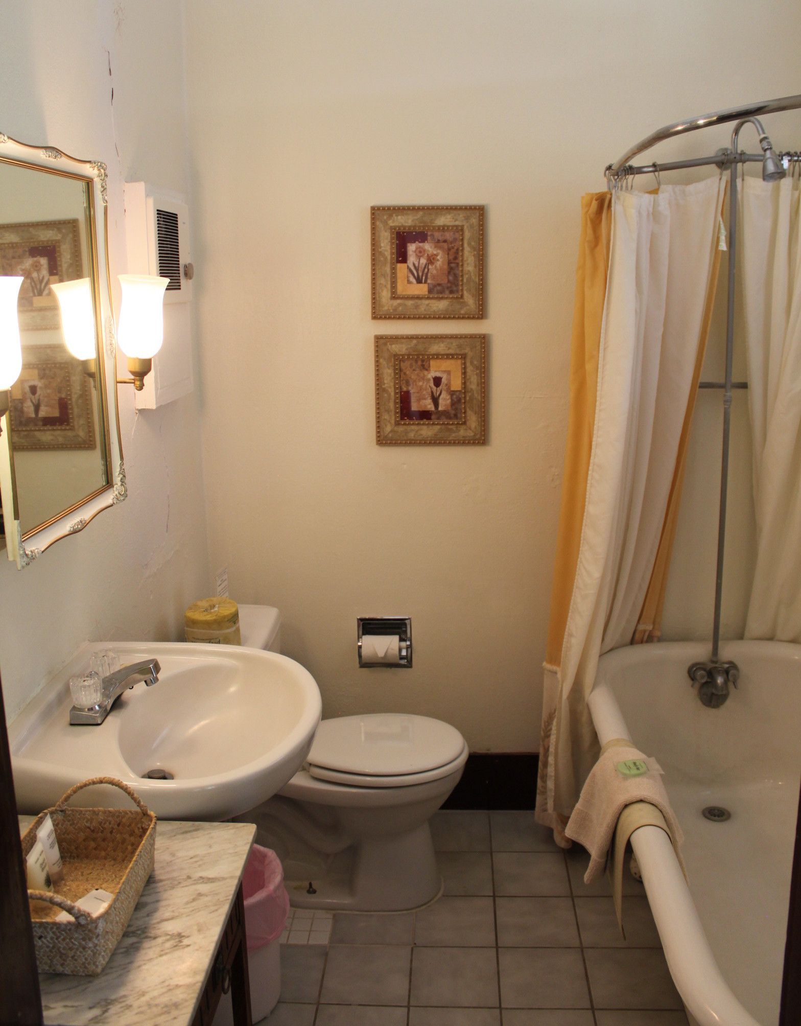 A bathroom with a sink, toilet, and bathtub. There are two framed pictures on the wall and a shower curtain.