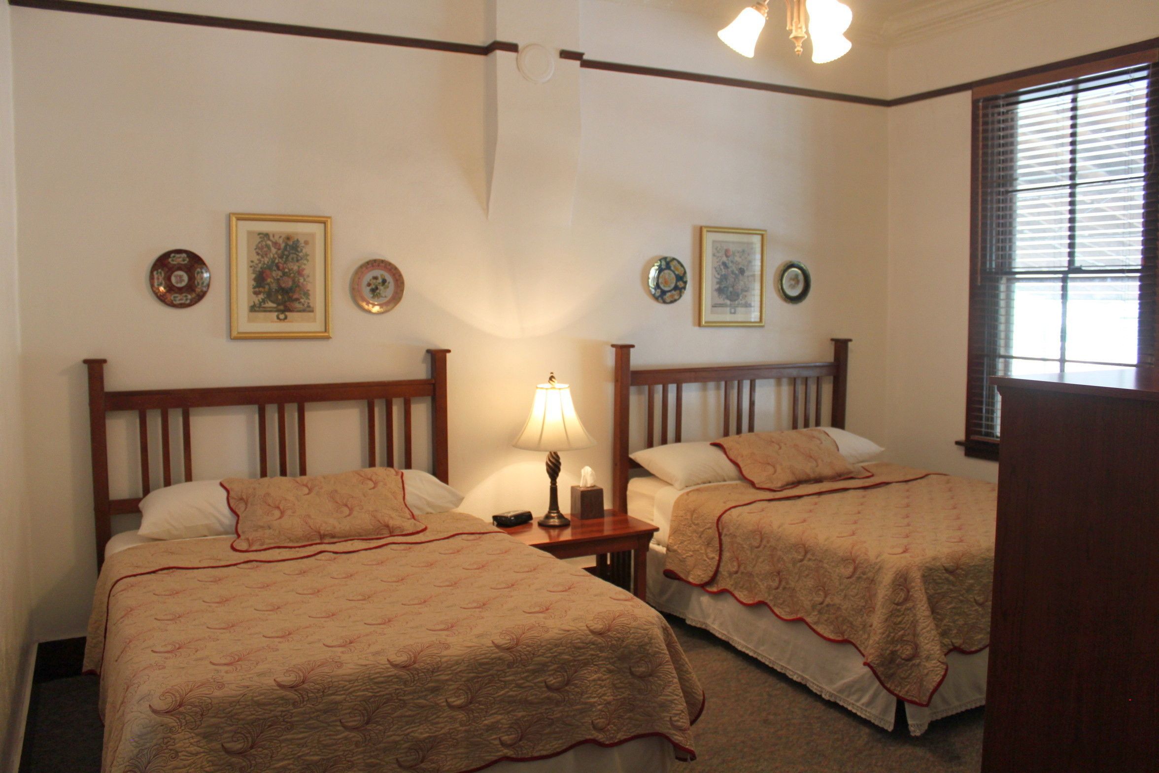 Una camera d'albergo con due letti, un comodino con una lampada e piatti decorativi appesi al muro.