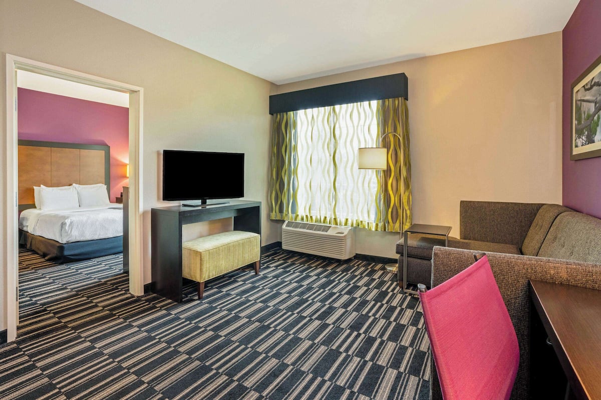 Habitación de hotel con cama, escritorio con televisor de pantalla plana, sofá y ventana con cortinas estampadas.