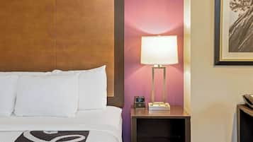 A hotel room with a bed, a nightstand with a lamp, a clock, and a framed picture on the wall.