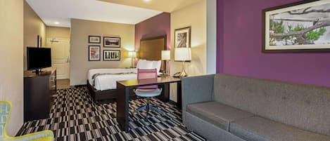 Una habitación de hotel con cama, escritorio, sofá y televisión.
