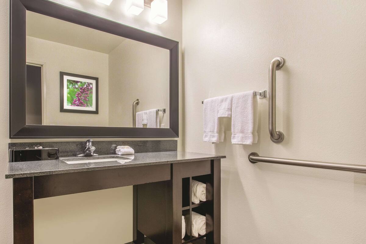 Un baño con un espejo grande, un lavabo, un perchero para toallas y un pasamanos.