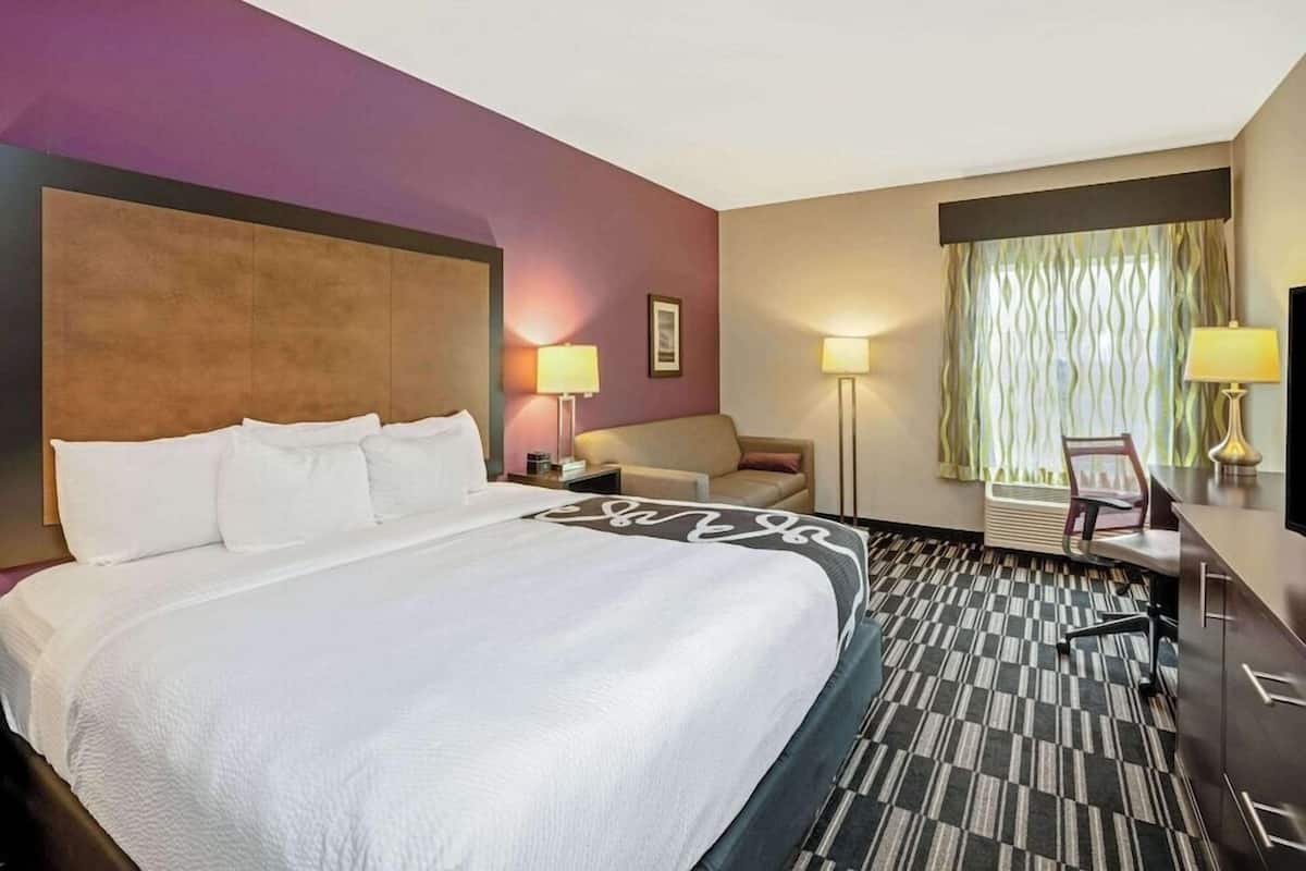 Habitación de hotel con una cama grande, un escritorio, una silla, una lámpara y una ventana con cortinas.